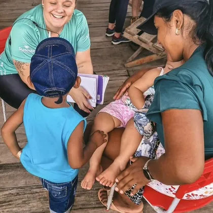 Luciene com prancheta conversando com uma família em um deck de madeira