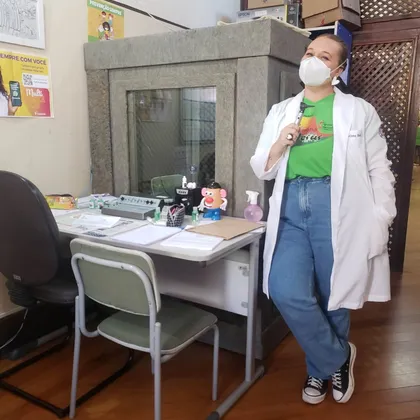 Luciene segurando um otoscópio ao lado da cabine acústica